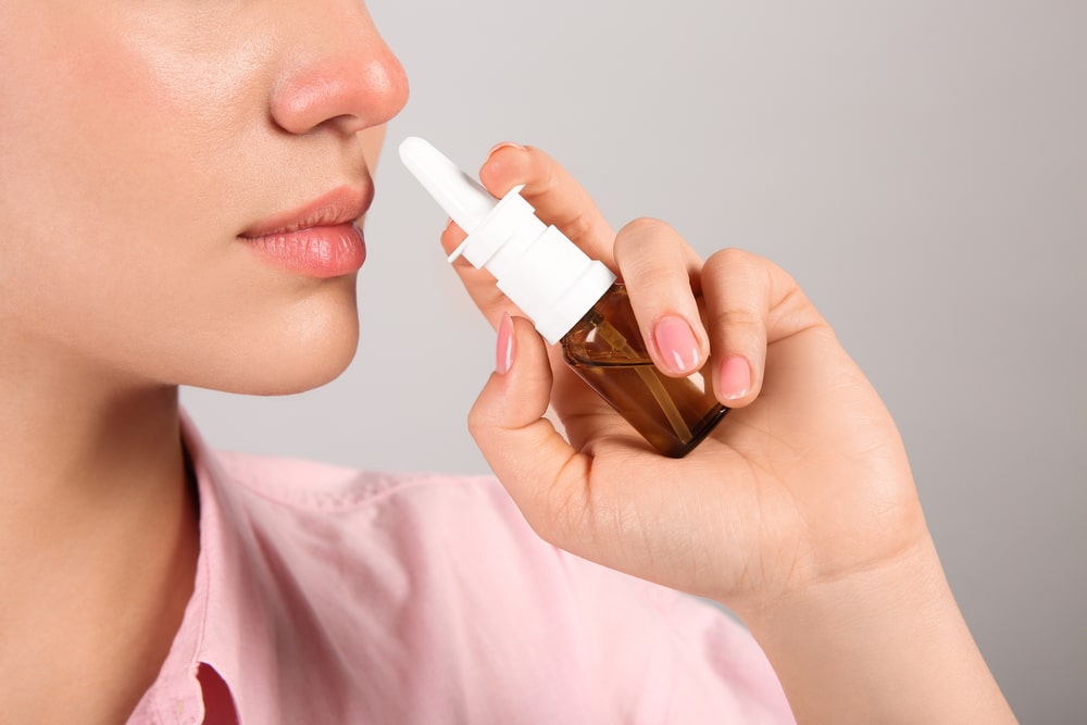 Woman using nasal spray on light grey background, closeup. Space
