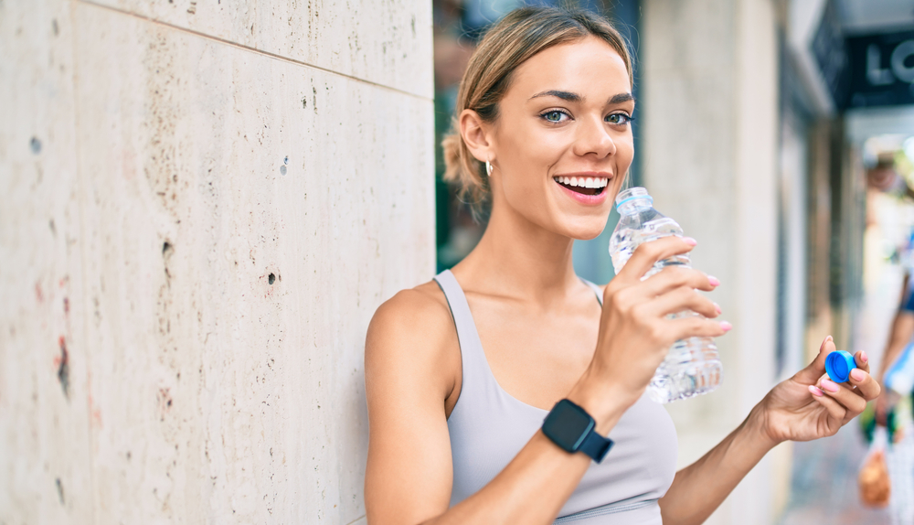 Woman in her 20s drinks a bottle of water while shopping at an outdoor mall.