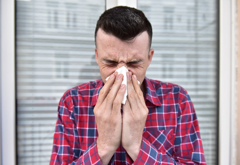 Man with recurrent sinus infection blows his nose into a tissue.
