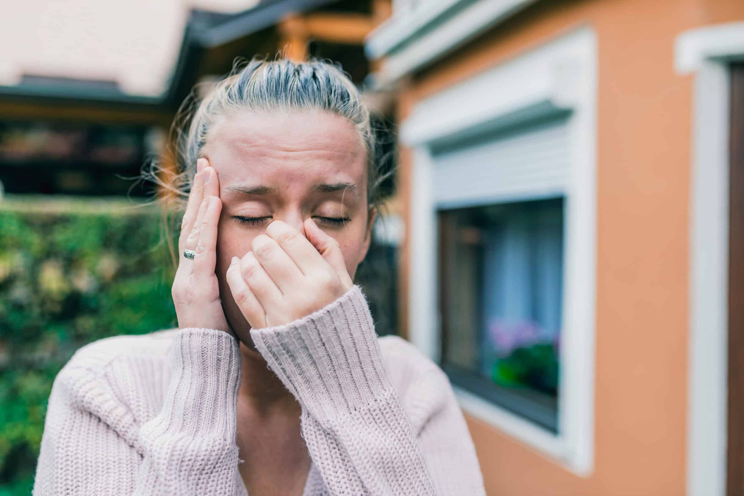 Woman outside holding her nose and head in pain due to sinus headache in the fall weather