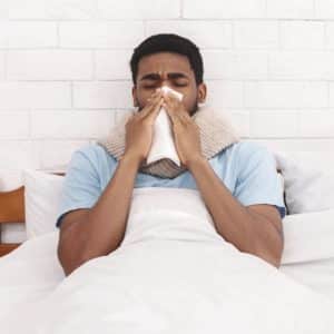 Sick african-american guy blowing his nose into paper napkin in bed
