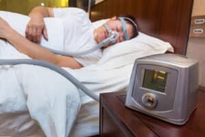 CPAP machine sitting on the bedside table next to the bed with sleeping Asian man